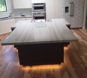 A kitchen with an island and lights on the counter.