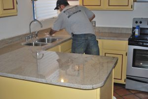 A man in grey shirt cleaning counter top.